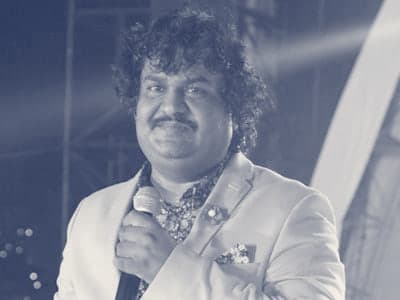 Osman Mir singing into a microphone on stage in a cream blazer, during a concert in the USA in 2014